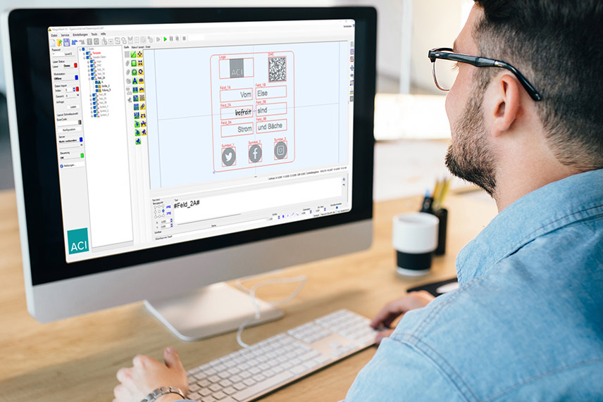 Young man sits in front of a PC and the software interface of Magic Mark, ACI's laser software, can be seen on the screen