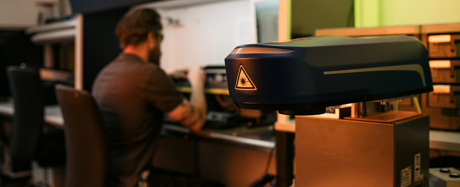 Équipe d'assistance ACI Laser dans le laboratoire : collaborateurs en arrière-plan, tête laser au premier plan