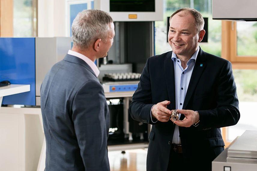 ACI Laser Vertriebsleiter mit Kunde und Musterteil, Showroom im Hintergrund