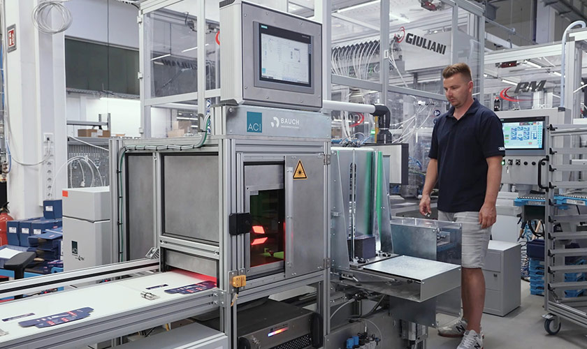 ACI Laseranlage in automatisierter Fertigungsumgebung mit integrierter Fördertechnik, Bedienpanel und Bediener neben der Anlage.